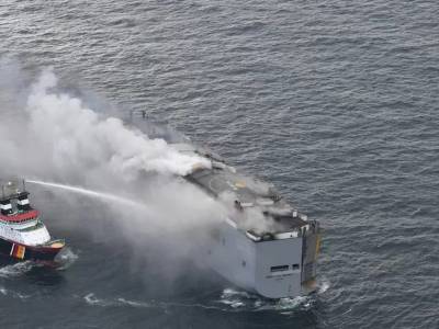 Burned-out car carrier under tow as fire subsides